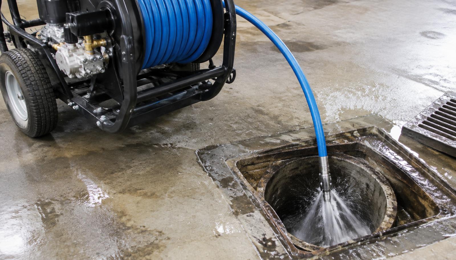 Hydro jetting machine blasting high-pressure water into a floor drain to scour the pipe clean